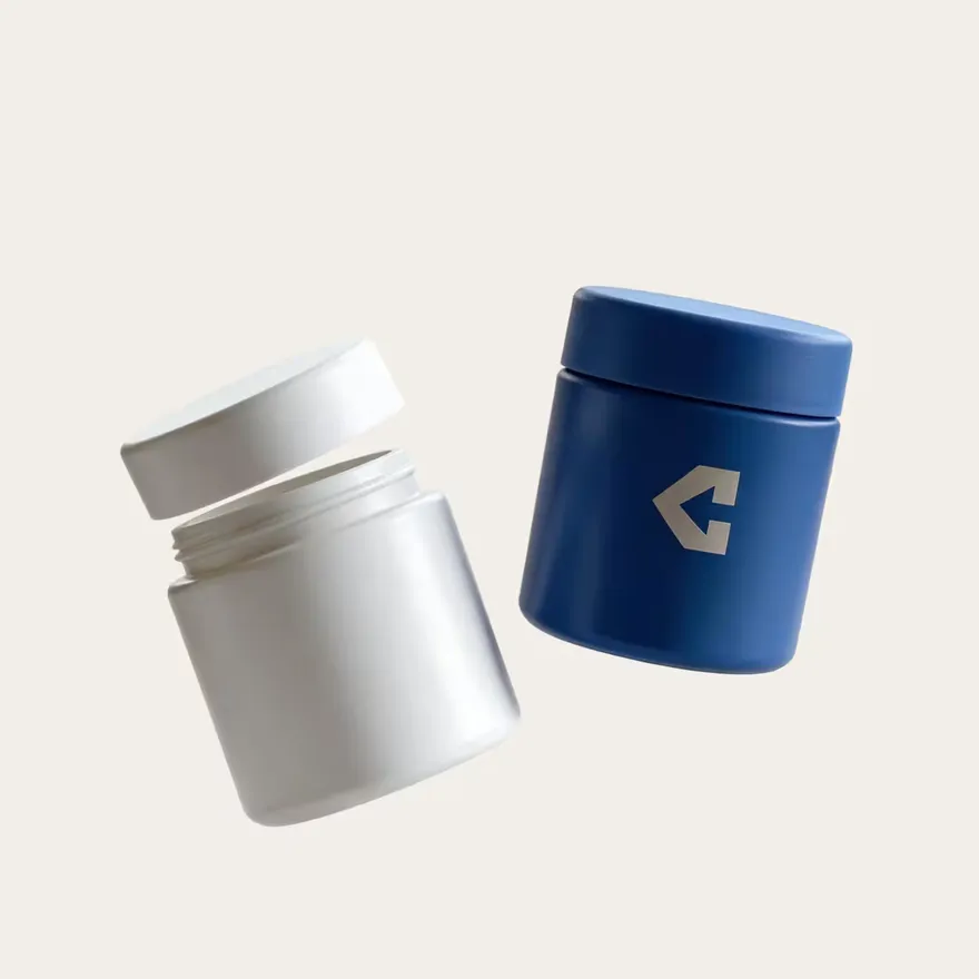 A white pharmacy bottle with its lid off beside a navy branded bottle.