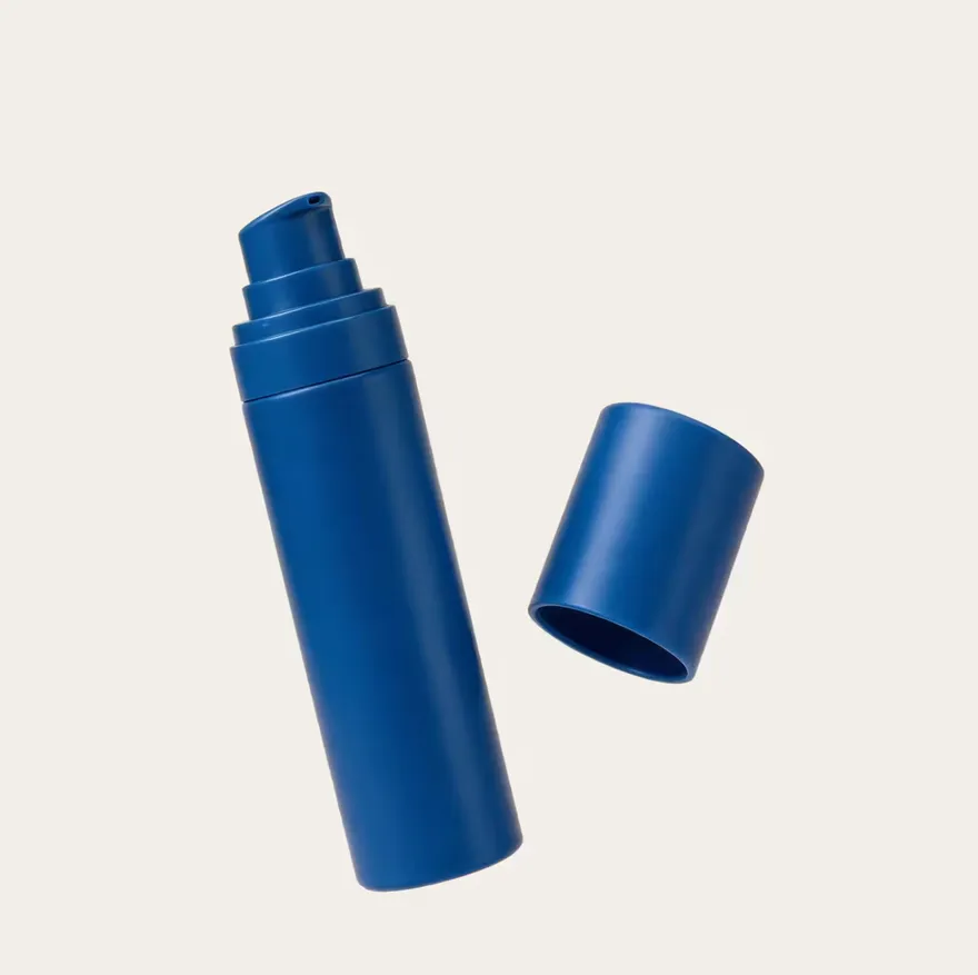 A navy airless pump bottle with its cap alongside.